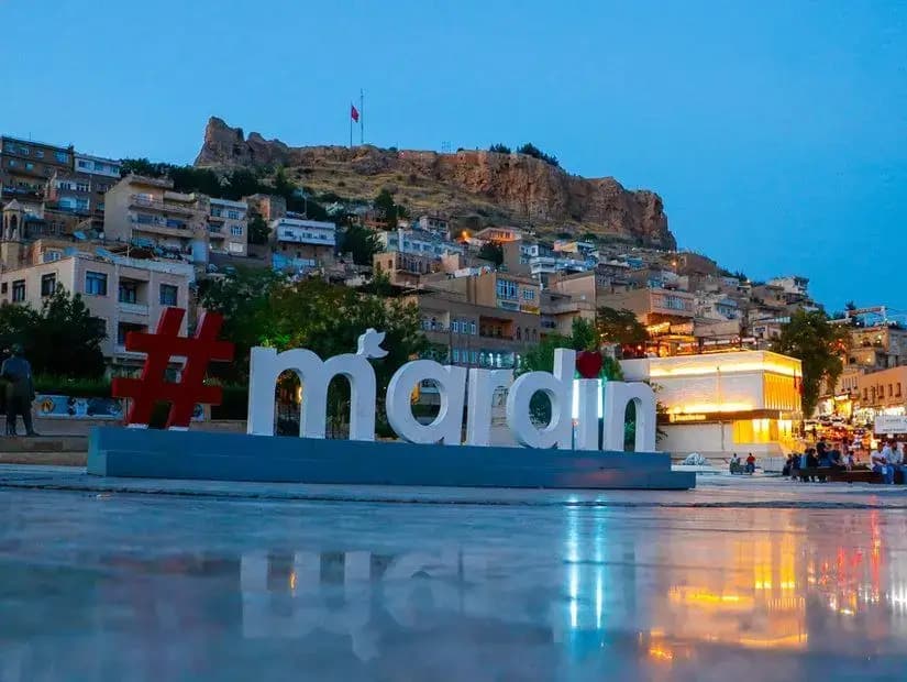 Akşam ışığında Cumhuriyet Meydanı'ndaki Mardin yazısı ve kale manzarası