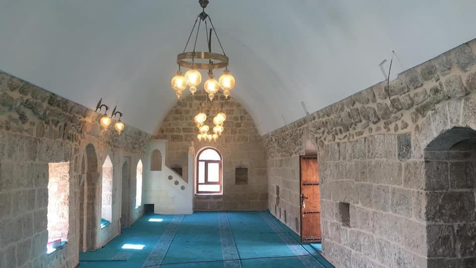 Emineddin Külliyesi'nde taş duvarlı iç mekan, mihrap, pencereler ve avizeler